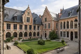 Courtyard of the Musée de l’Hospice Comtesse with historic brick and stone Flemish-style buildings, trimmed lawn, and benches in soft daylight.